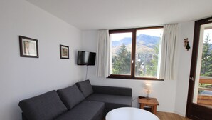 Ein modernes Wohnzimmer mit einem grauen Sofa, einem weißen Tisch und einem an der Wand befestigten Fernseher.