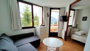 Ein Zimmer mit einer Couch, einem kleinen runden Tisch, einem Bett, einem Fernseher und Blick auf Grün.