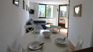 Ein Essbereich mit einem runden Tisch für vier Personen, einer Couch im Hintergrund und einem Balkon mit Blick.