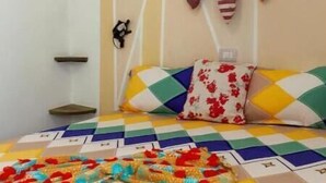Una cama con un colcha colorida, un cabecero con adornos colgantes y un almohadón estampado con flores.