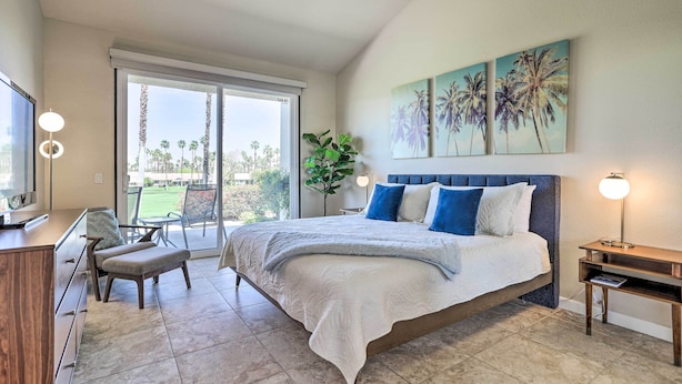 A bedroom with a large bed, a desk, a chair, and a TV. There is a sliding glass door leading to a balcony with a view of palm trees. - Mtn & Golf Course Views: Relaxing Palm Desert Gem (Palm Desert)