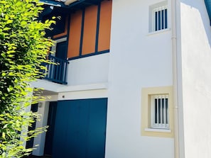 A two-story building with a balcony, a large blue door, and a small window.