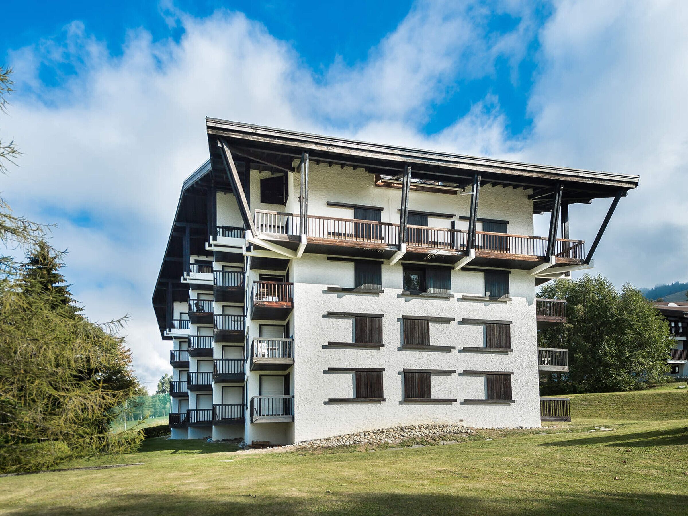 A multi-story building with balconies, a sloped roof, and a stone base.