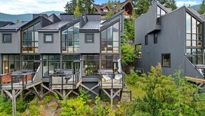 A modern multi-story building with large windows and a deck area. - 3BR Townhouse • AC • Fireplace • Lake & Trail Views • 6-Min to Gondola (Whistler)