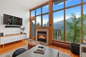 Un salon moderne doté d’une cheminée, de grandes fenêtres et offrant une vue sur les montagnes.