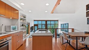A modern kitchen with wooden cabinets, a central island, and a dining area with a wooden table and chairs. - 3BR Townhouse • AC • Fireplace • Lake & Trail Views • 6-Min to Gondola (Whistler)