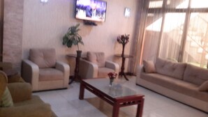A living room with two sofas, a coffee table, and a TV mounted on the wall. - Mesfin Harar Hotel (Addis Ababa)