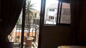 A room with a balcony, a potted plant, and a view of neighboring buildings. - Mesfin Harar Hotel (Addis Ababa)