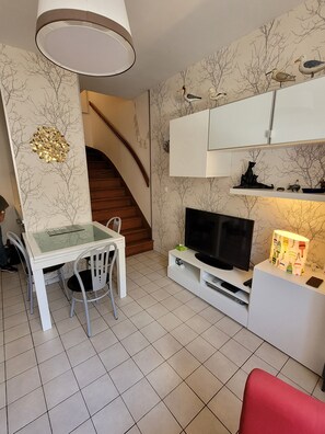 A modern living room with a dining area, a staircase, and a TV on a white cabinet. - Duplex apartment in the heart of La Roche Bernard (La Roche-Bernard)