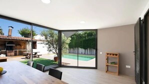 Eine moderne Küche mit Einbauofen, einem Essbereich mit Holztisch und einer Glasschiebetür, die in einen Garten mit Pool führt.