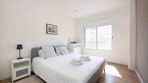 Ein Schlafzimmer mit Bett, Nachttisch, Lampe, Fenster und einem gerahmten Bild an der Wand.