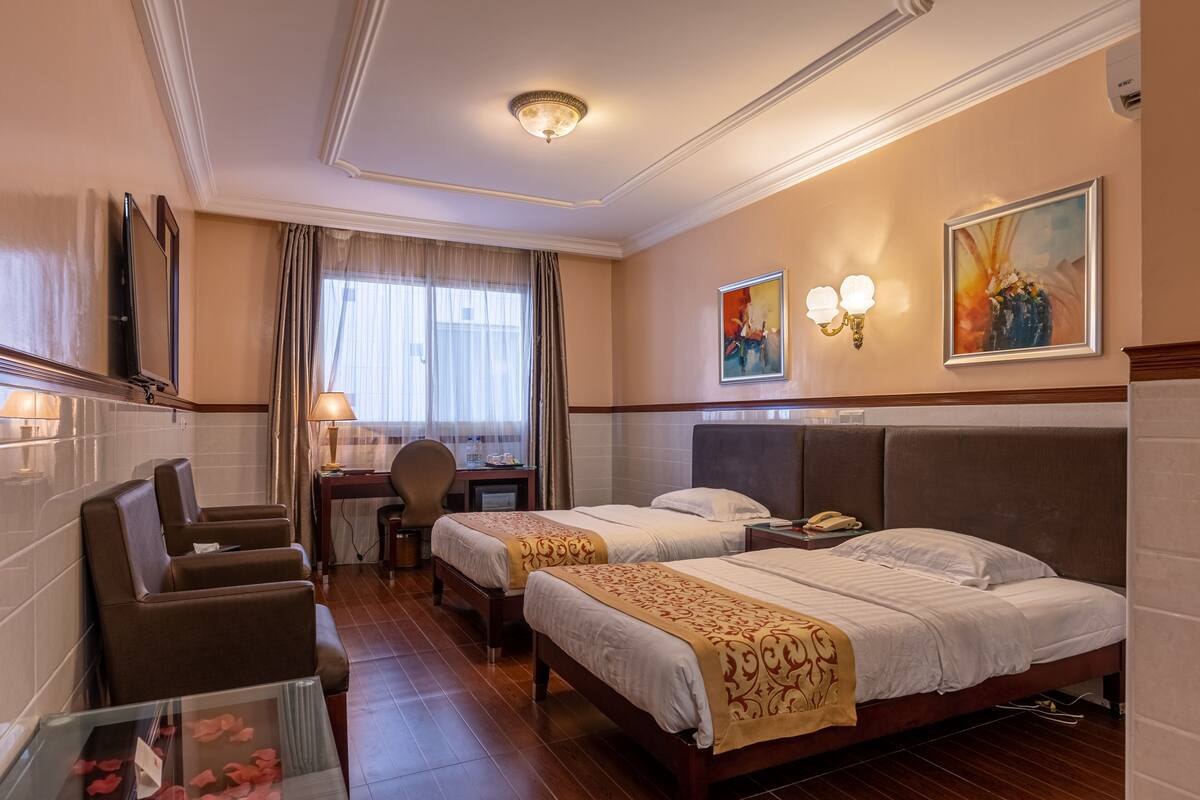A hotel room with two beds, a desk, a chair, and a glass table with rose petals.