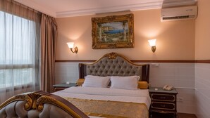 A hotel room with a large bed, two bedside tables, a nightstand, and a wall-mounted air conditioner. - L'Etoile d'Or Hotel London (Libreville)