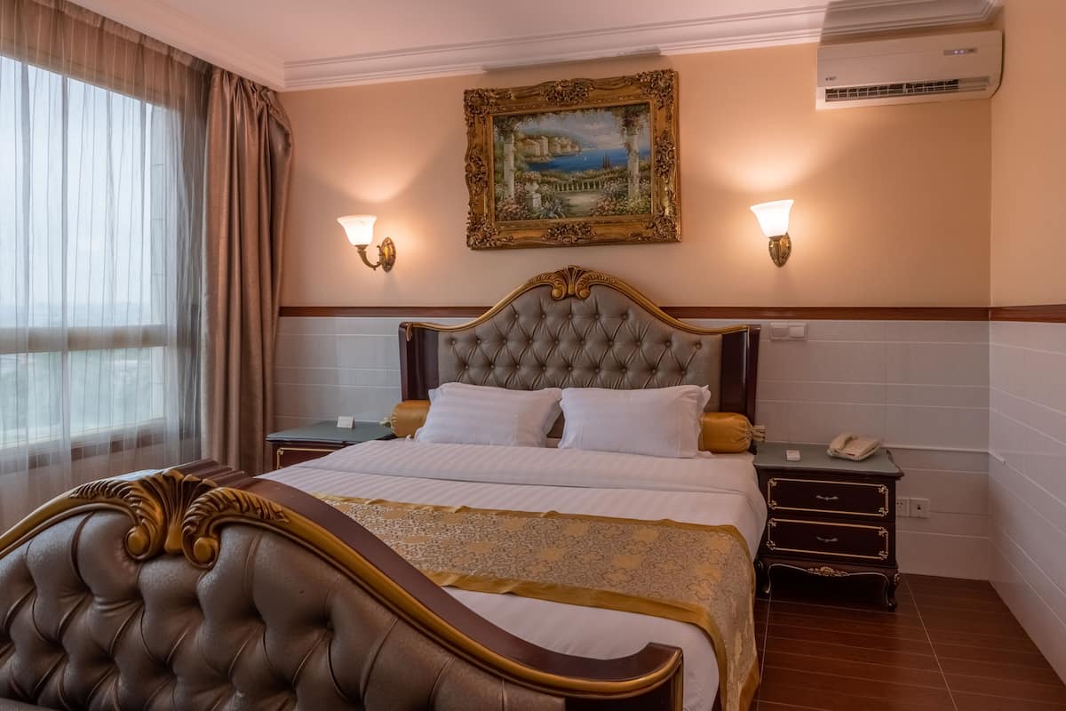 A hotel room with a large bed, two bedside tables, a nightstand, and a wall-mounted air conditioner.