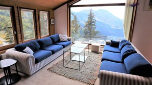 A modern living room with a large sofa, a coffee table, and a view of mountains through large windows.