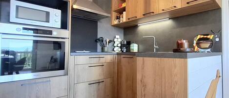 Una cocina moderna con armarios de madera, horno empotrado, microondas y campana extractora de acero inoxidable.