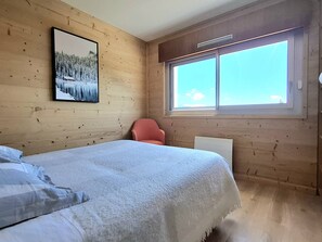 A bedroom with a bed, a chair, a window, and a framed picture on the wall. - Renovated 2-Star Apartment for 4, Balcony, Parking, Ski Storage, No Pets, No Smoking (Bolquère-Pyrénées 2000)