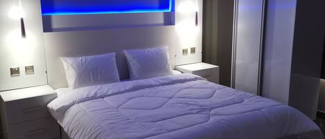 A modern bedroom with a large bed, white bedding, a blue accent wall, and a wardrobe.