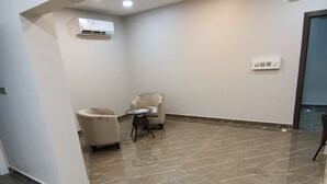 A modern room with a marble floor, a white air conditioning unit, a small round table, and a beige armchair. - MARINA SOHAR HOTEL (Sohar)