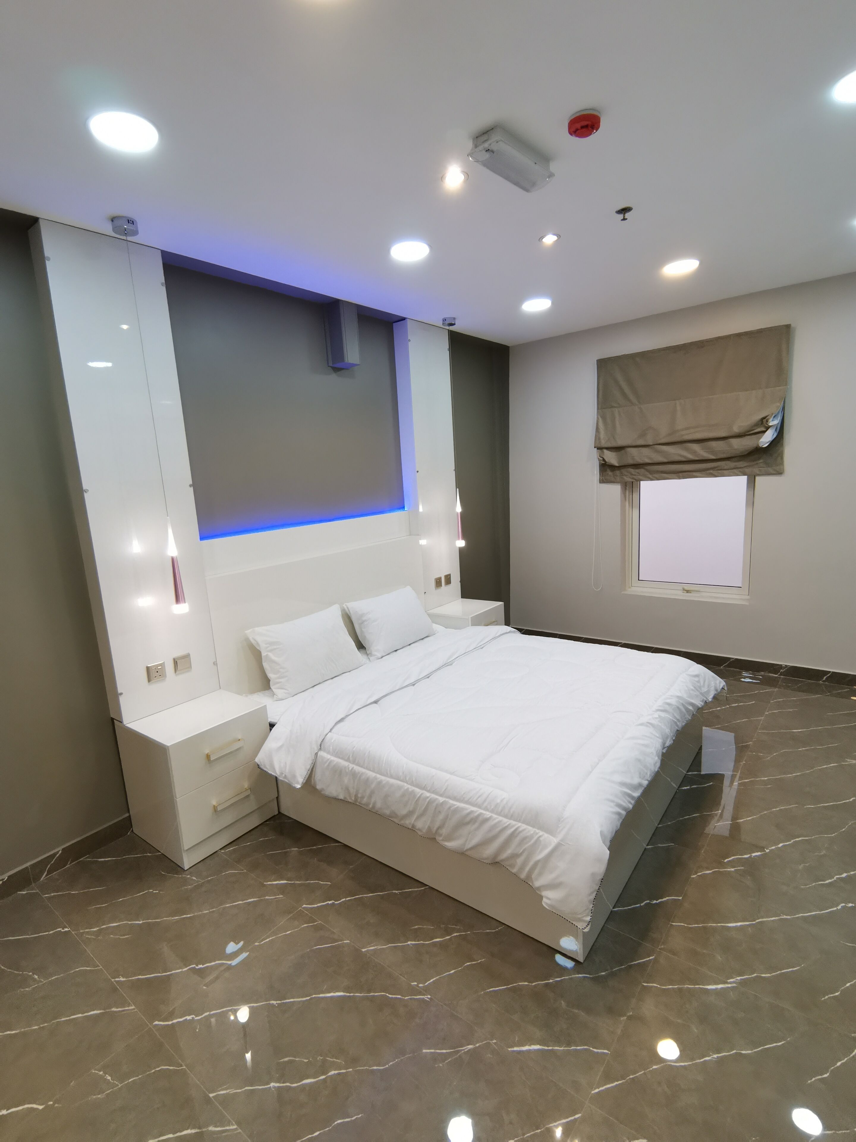 A modern bedroom with a large bed, bedside tables, a wall-mounted light, and a window with a blind.