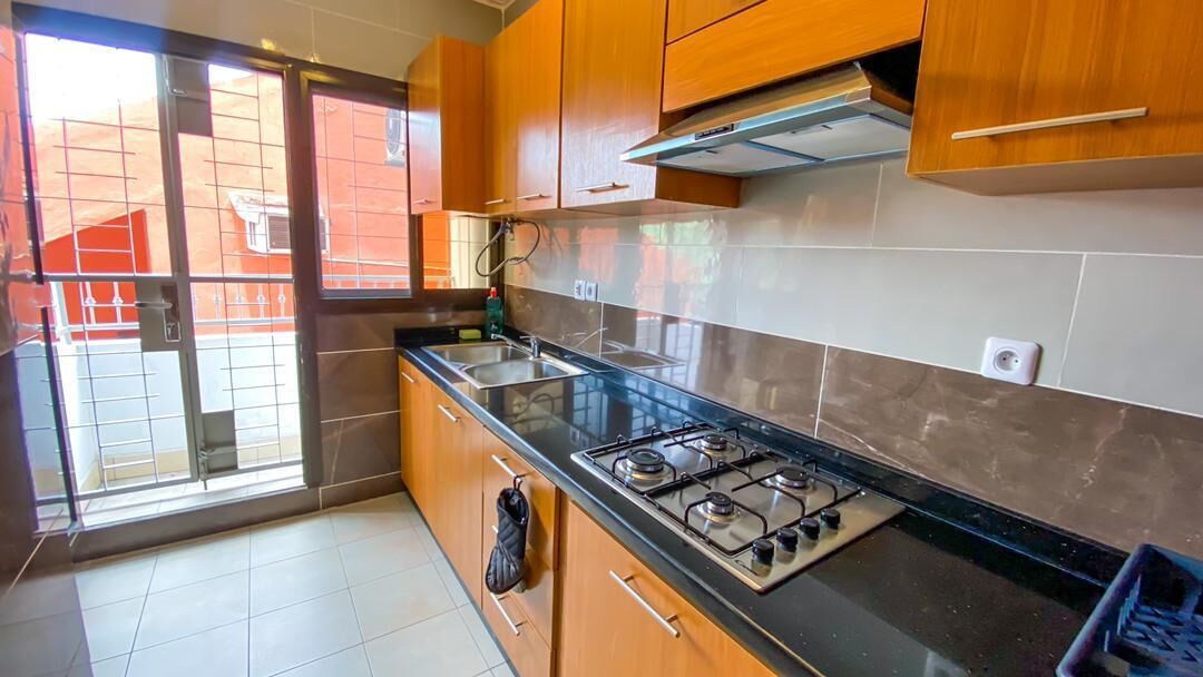 A kitchen with wooden cabinets, a gas stove, and a window with a view of a red building.