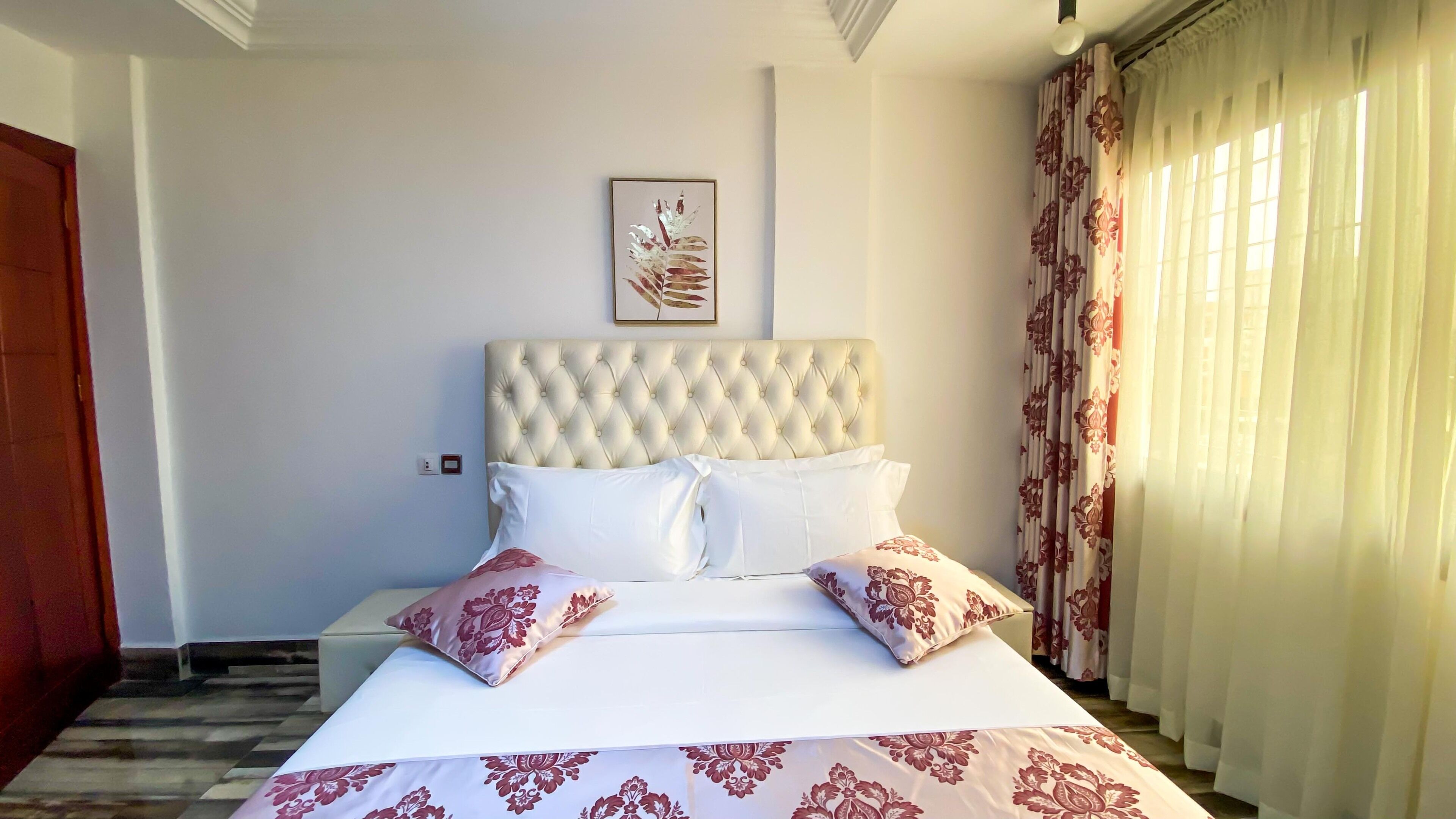 A neatly made bed with a tufted headboard, white bedding, and floral-patterned pillows.
