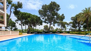 A swimming pool with clear blue water, surrounded by trees and a building with a balcony. - AirCon Apartment · Sea Views  · Pool · UHC CALA DORADA (Salou)