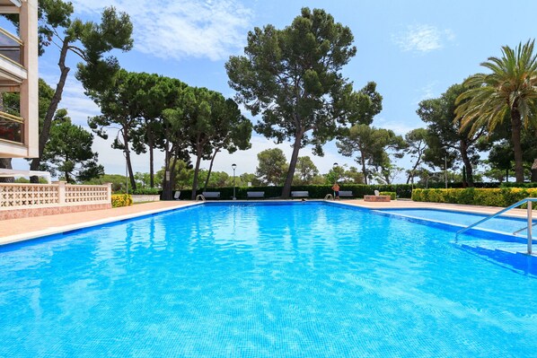 Une piscine à l’eau d’un bleu cristallin, entourée d’arbres et bordée d’un bâtiment doté d’un balcon.