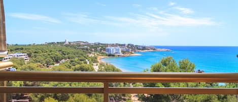 Une vue sur la côte depuis un balcon, avec un ciel dégagé, une plage et des bâtiments visibles au loin.