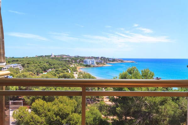 A coastal view from a balcony with a clear sky, a beach, and buildings in the distance.
