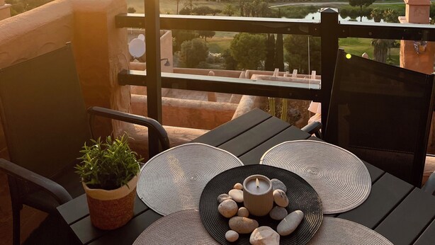 Uma varanda com mesa posta para um chá, com vista para uma paisagem deslumbrante, campos e colinas ao longe ao pôr do sol.
