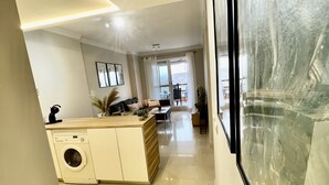 Uma cozinha moderna com máquina de lavar embutida, sala de jantar com mesa e cadeiras, e uma janela grande que oferece vista para o exterior.