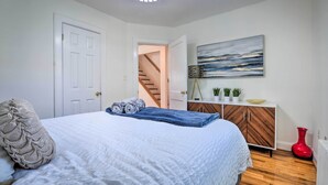 A bedroom with a bed, a dresser, a painting, and a red vase.