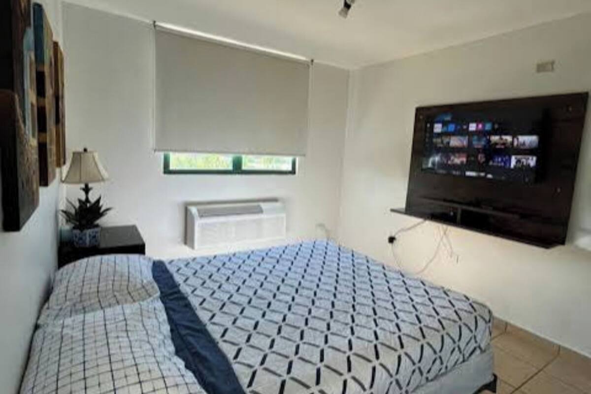 A bedroom with a bed, a TV, a window, and a ceiling fan.