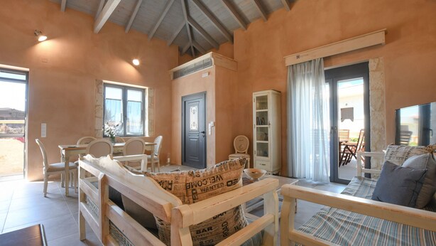 A cozy room with a wooden bed, a sofa, a dining table with chairs, and a cabinet. - Arismari Villa - Private Pool (Hersonissos)