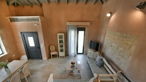 A cozy living room with a sofa, a dining table with chairs, a TV, and a stone wall. - Arismari Villa - Private Pool (Hersonissos)