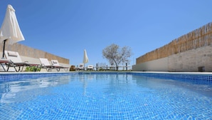 A clear blue pool with lounge chairs and umbrellas, surrounded by a stone wall and a tree. - Arismari Villa - Private Pool (Hersonissos)