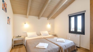 A bedroom with two beds, wooden ceiling beams, a window, and a radiator. - Arismari Villa - Private Pool (Hersonissos)