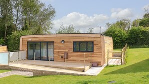 A modern wooden cabin with a deck, large sliding glass doors, and a small window. - Pinot (Ryde)