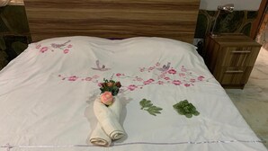Ein ordentlich bezogenes Bett mit floraler Tagesdecke, einem aufgerollten Handtuch und einem kleinen Blumenstrauß.