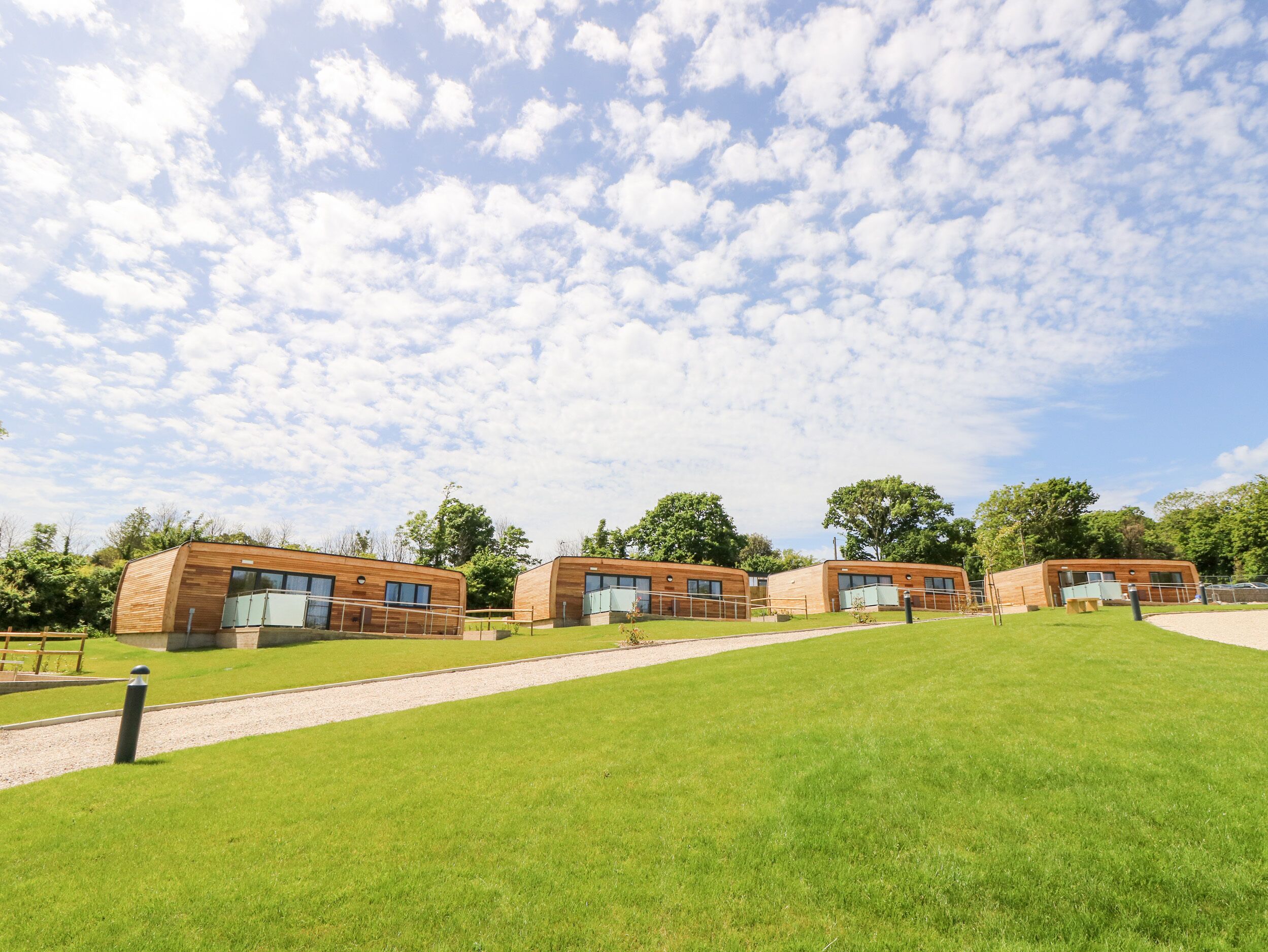 A row of modern wooden cabins with large windows, set on a grassy field with a clear sky.