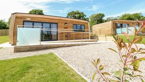 A modern wooden building with large windows and a glass door, surrounded by gravel and grass. - Amarone (Ryde)