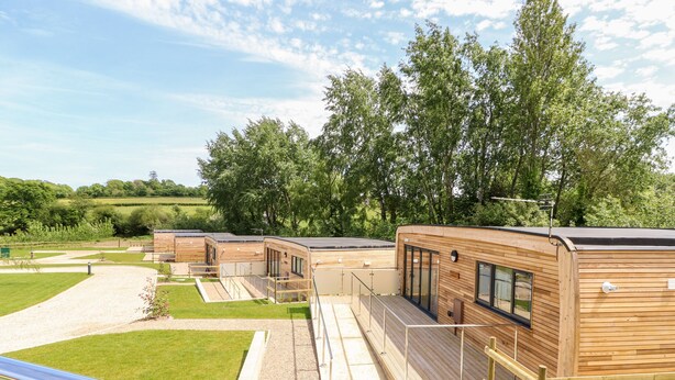 A row of modern wooden cabins with balconies, set in a grassy area with trees in the background. - Amarone (Ryde)