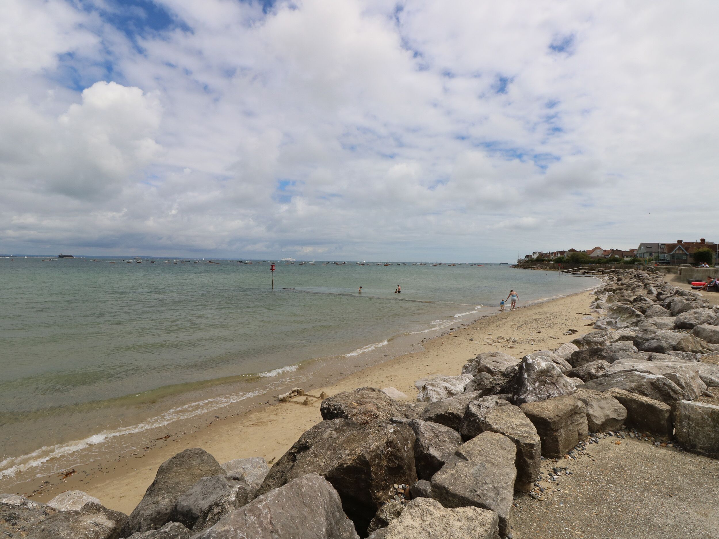 A beach with a rocky shoreline, calm water, and a few people in the distance.