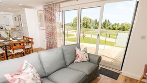 A modern living room with a grey sofa, floral cushions, and a dining area with wooden furniture. - Amarone (Ryde)