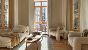 Uma sala de estar ampla, com uma janela grande, um sofá, uma poltrona e uma mesa de centro.