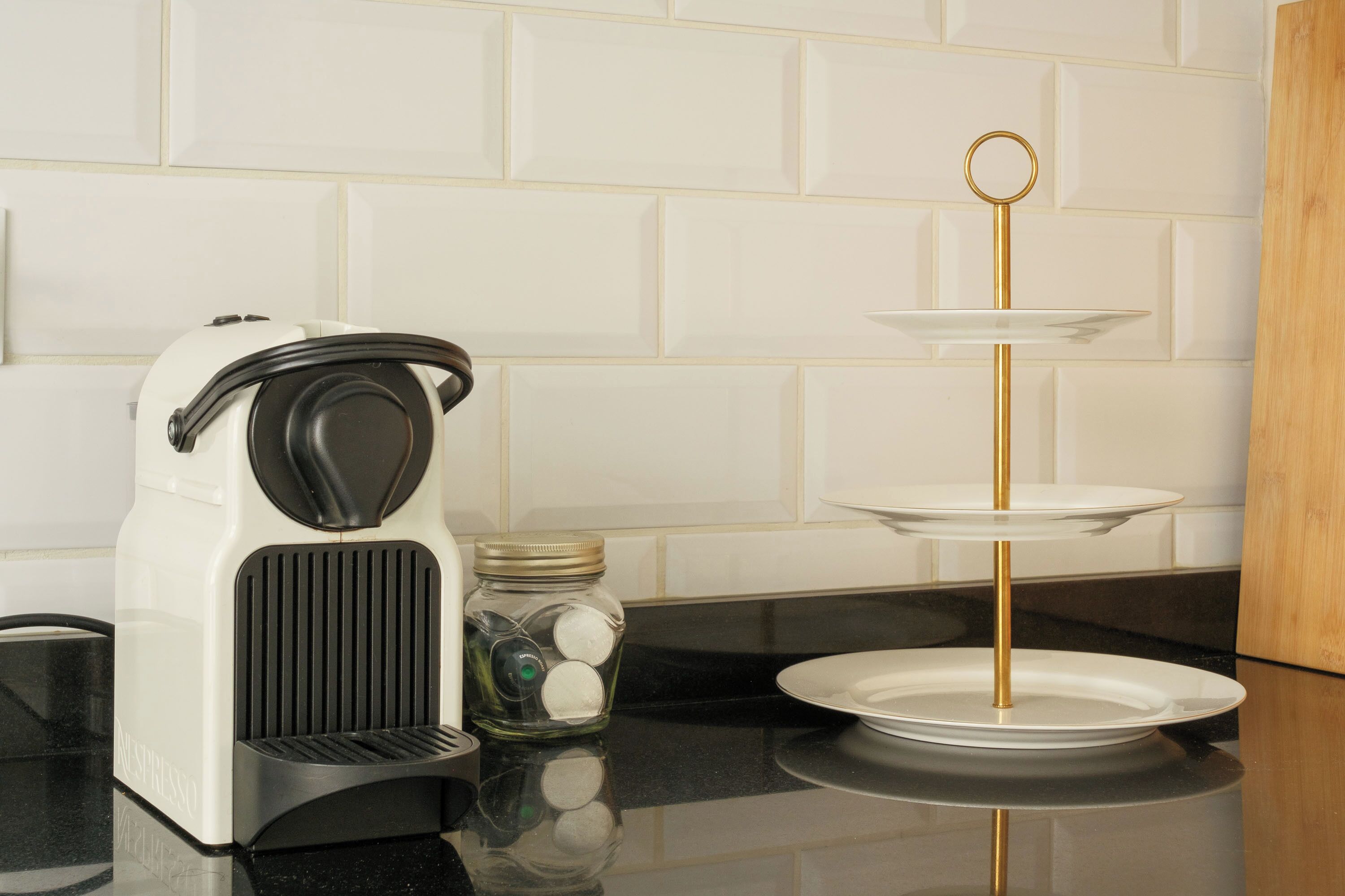 Una encimera de cocina con una cafetera, un tarro de monedas y un expositor blanco de tres niveles.