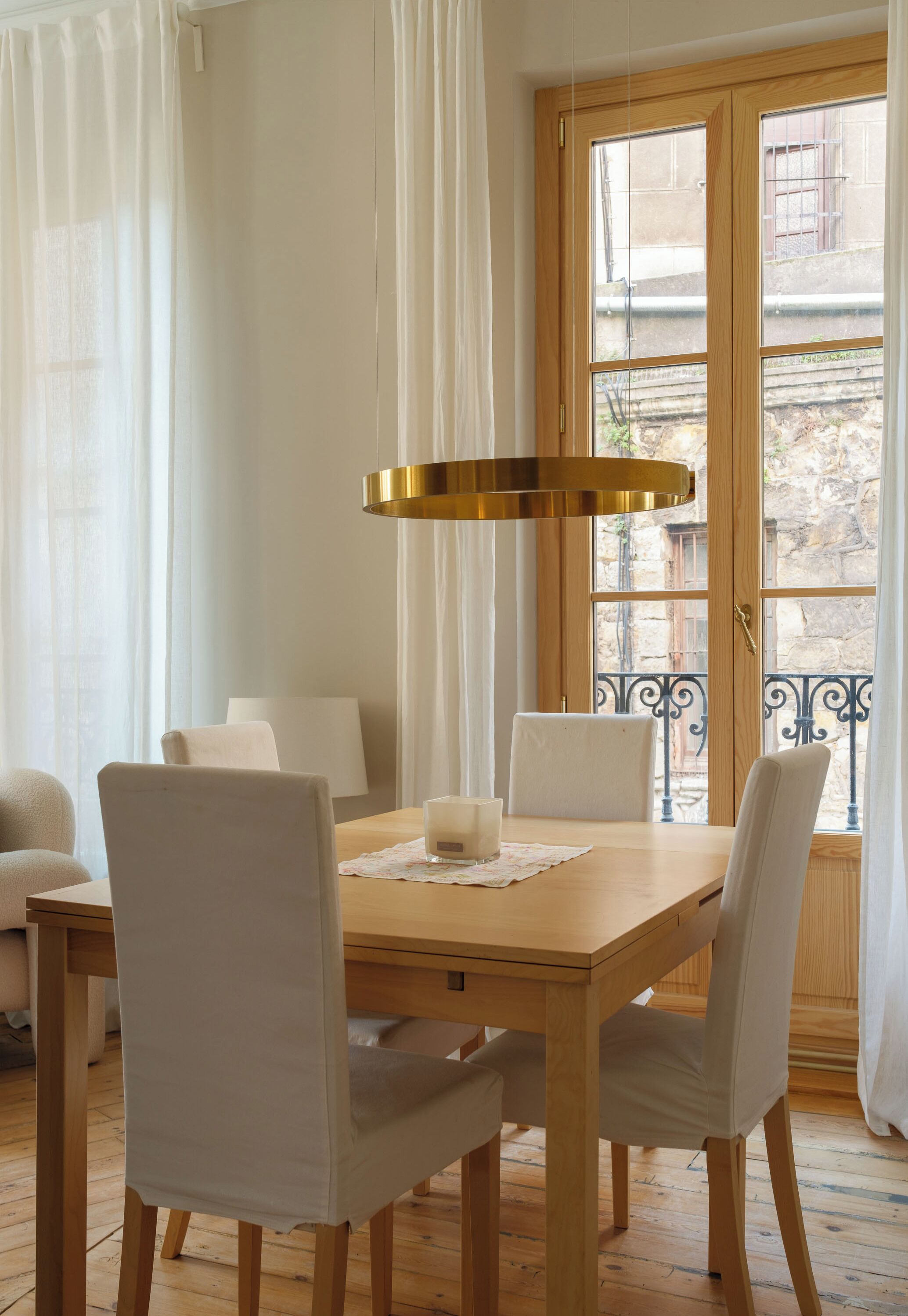 Un comedor con mesa de madera, cuatro sillas, una vela y una lámpara colgante.