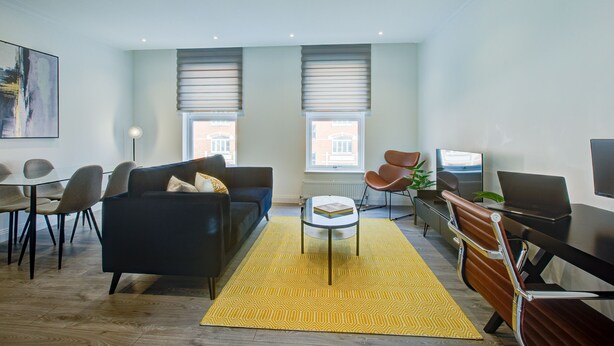 Een moderne woonkamer met een bank, salontafel en een eethoek met stoelen.