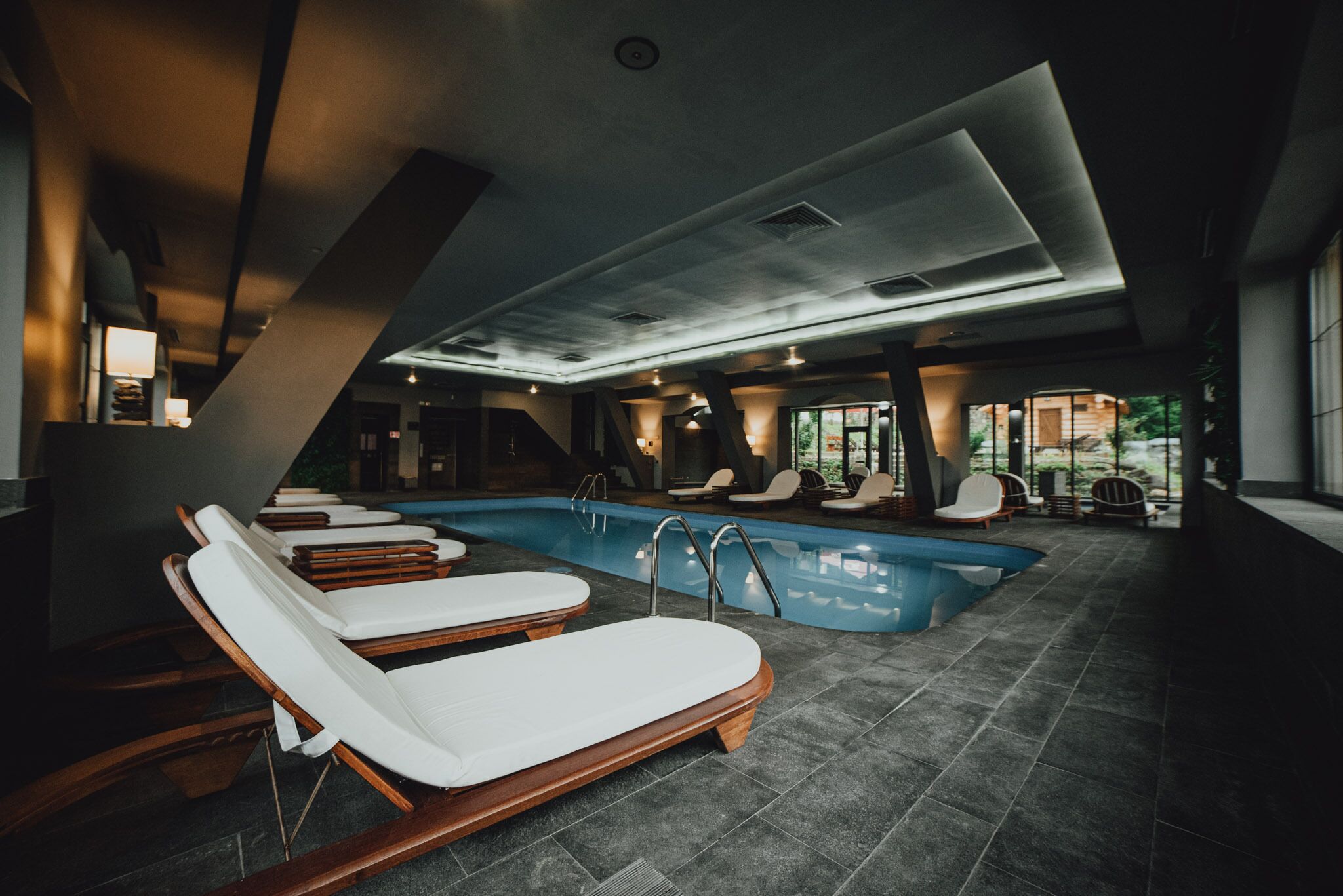 A modern indoor pool area with lounge chairs and a clear view of the pool.
